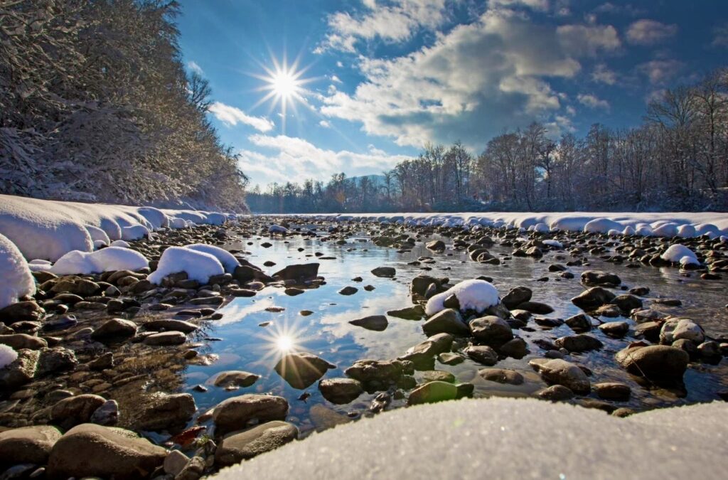 Winterlicher Flusslauf mit Schnee und Sonnenstern